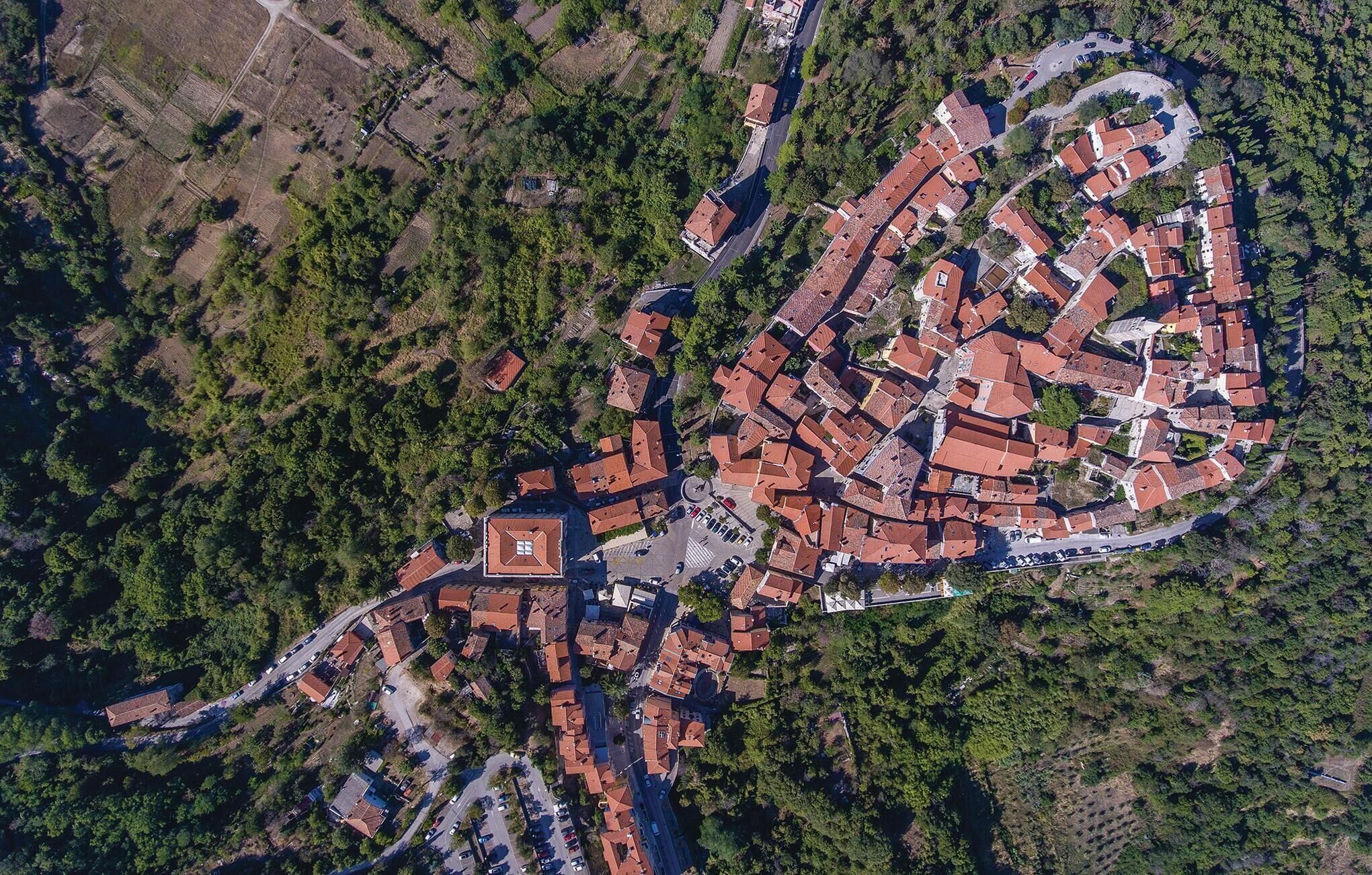 Luchtbeeld van een stad met een centraal plein, omringd door gebouwen met rode pannendaken en weelderige groene gebieden.