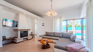 Een moderne woonkamer met een grote bank, een houten salontafel, een open haard en een aan de muur bevestigde televisie.
