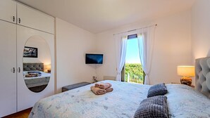 Een slaapkamer met een bed, een televisie, een raam met gordijnen, een nachtkastje en een kledingkast.