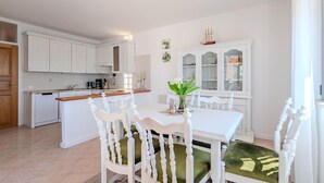Een moderne keuken met witte kasten, een eettafel met witte stoelen en een klein kookeiland.