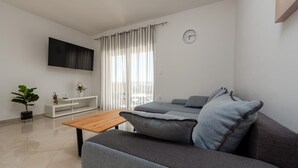 A modern living room with a grey sofa, a wooden coffee table, a white console table with a plant, and a TV mounted on the wall. - Amazing apartment in Maslenica with WiFi (Maslenica)
