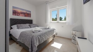 A bedroom with a bed, a painting, a window with curtains, a remote control, and a white wall. - Amazing apartment in Maslenica with WiFi (Maslenica)