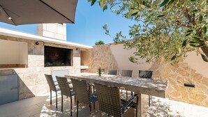 An outdoor patio with a stone wall, a grill, and wicker furniture. - Amazing apartment in Maslenica with WiFi (Maslenica)