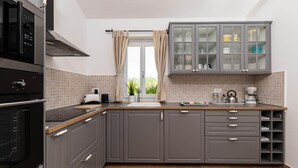 Een moderne keuken met grijze kastjes, een inbouwoven, een raam met gordijnen en een koffieapparaat.