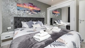 A modern bedroom with a large bed, grey and white bedding, a grey headboard, and a grey textured wall.