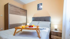 A neatly made bed with a tray of breakfast items, a bedside table with a lamp, and a framed picture on the wall.