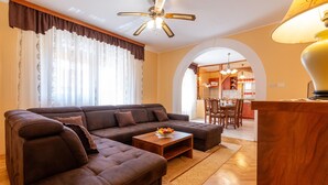A living room with a sectional sofa, a coffee table with fruit, and a dining area visible through an archway.