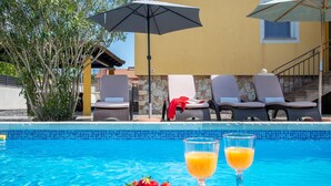 A poolside area with lounge chairs, a table with fruit and drinks, and umbrellas.