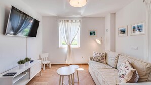 A modern living room with a flat-screen TV, a sofa with floral cushions, a small table, and a window with curtains. - Gorgeous home in Visnjan with private swimming pool, can be inside or outside (Visnjan)