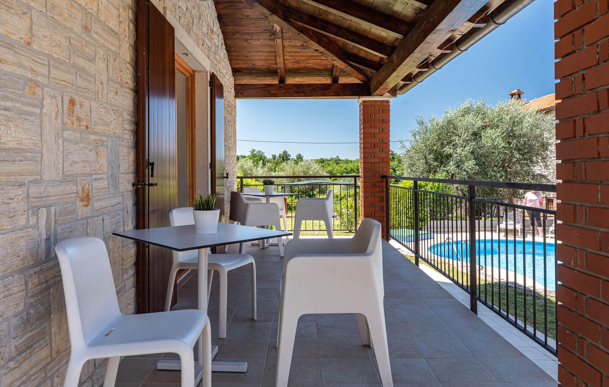 A covered outdoor area with a pool, white plastic chairs, and a table with a potted plant.