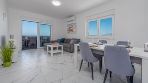 A modern living room with a dining area, large windows, and a view of the sea.