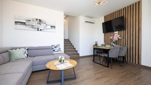 Un salon moderne avec un canapé gris, une table basse ronde en bois et un coin repas comprenant une table et des chaises en bois.