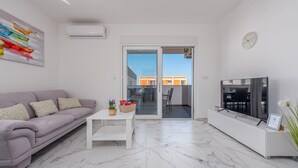 A modern living room with a sofa, a coffee table, a TV, and a balcony with a view of buildings. - 2 bedroom amazing apartment in Povljana (Povljana)