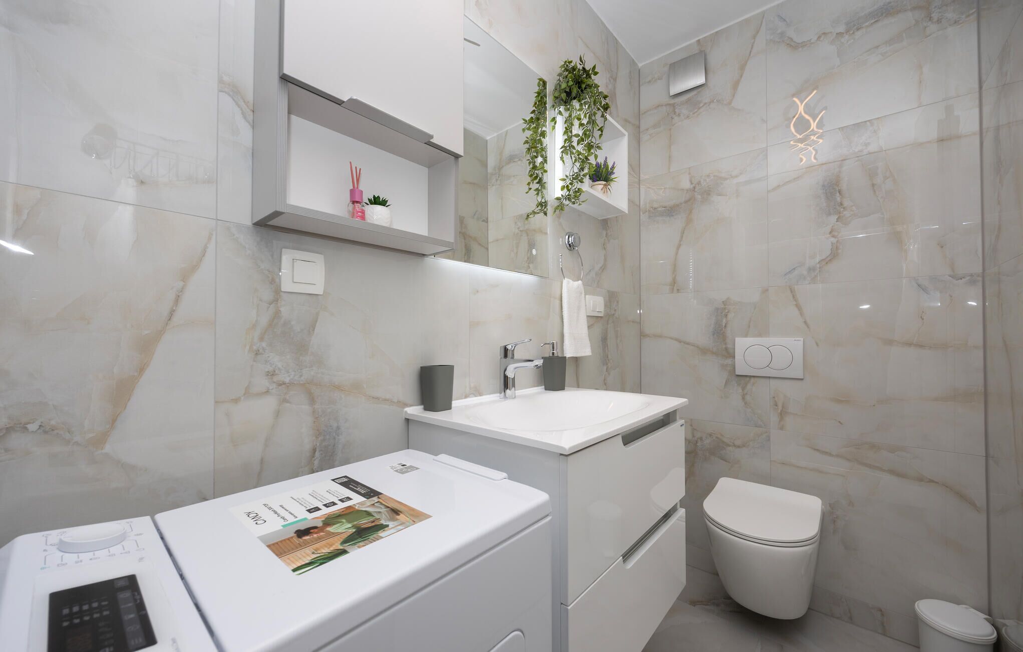 A modern bathroom with a white sink, a toilet, and a built-in washing machine.