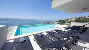 A rooftop infinity pool with lounge chairs and a clear view of the sea.