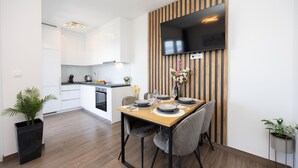 A modern kitchen with white cabinets, a wooden dining table set with plates, glasses, and a vase of flowers.