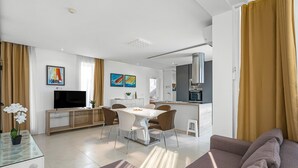 Ein modernes Wohnzimmer mit einer Couch, einem Essbereich mit Tisch und Stühlen, einem Fernseher und Kunstwerken an den Wänden.