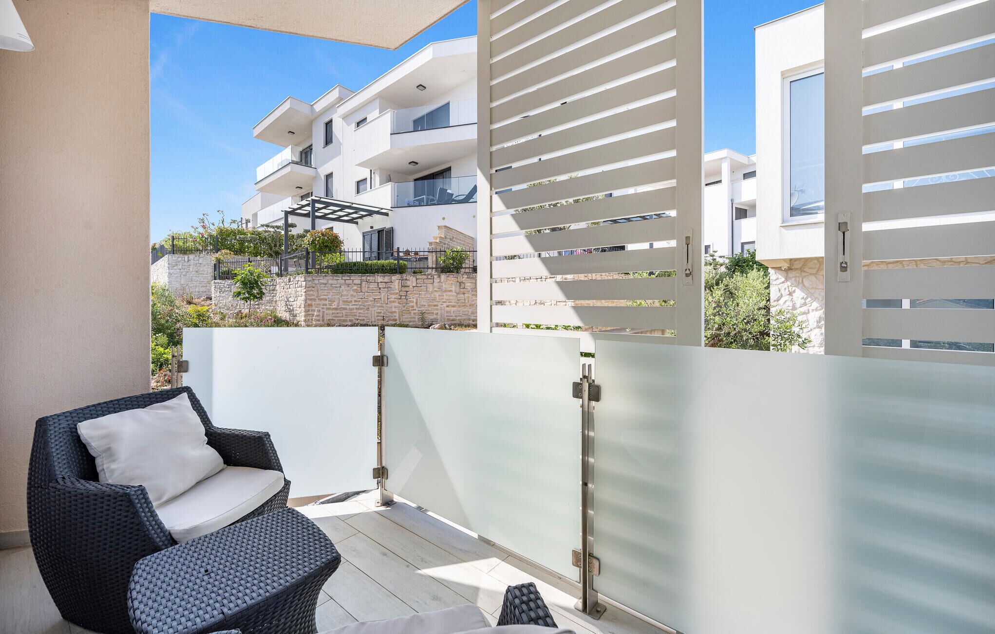 En balkon med en fletstol og en glasdør, der fører til en moderne lejlighedsbygning.