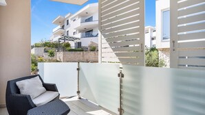 Un balcón con una silla de mimbre y un ventanal de vidrio que da a un edificio de apartamentos moderno.