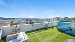 Terraza en la azotea con vistas a un puerto deportivo y montañas lejanas, una piscina pequeña y mobiliario de exterior.