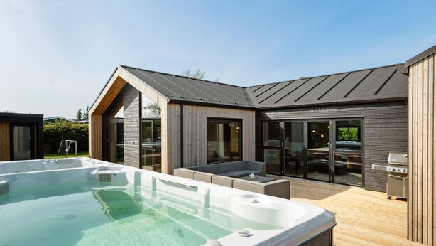 A modern outdoor swimming pool with a hot tub, wooden deck, and a barbecue area.