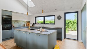 A modern kitchen with a central island, built-in appliances, and large windows offering a view of greenery.