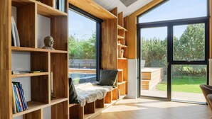 A modern interior with wooden bookshelves, a fur-covered bench, and large windows offering a view of greenery.