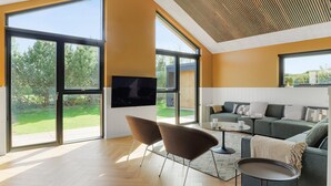A modern living room with large windows, a flat-screen TV, a sofa, and a coffee table.