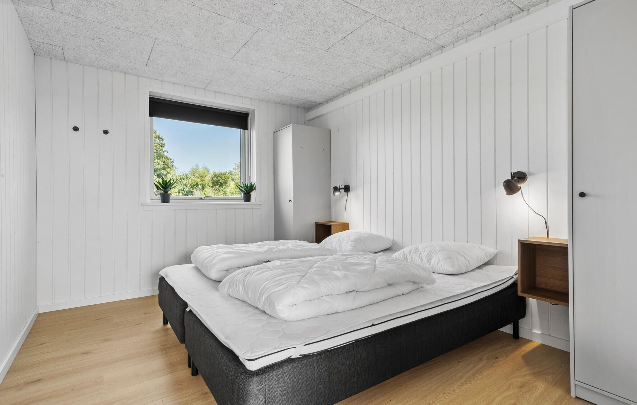 Une chambre à coucher avec un lit, une fenêtre, une table de chevet, une lampe et une armoire.
