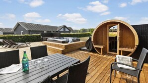 Une terrasse en bois avec des sièges d’extérieur, un jacuzzi et un sauna.