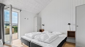 Une chambre à coucher moderne avec un grand lit, une porte-fenêtre coulissante donnant sur un balcon et un design minimaliste.