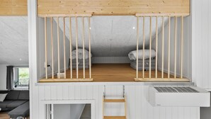 Une chambre mansardée avec un plafond en pente, deux lits, une échelle en bois et un appareil de climatisation blanc.