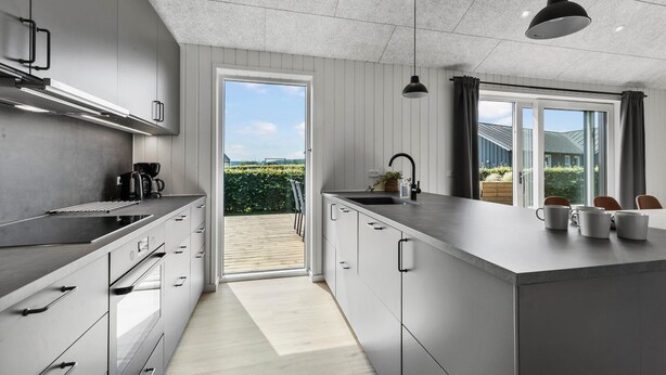 Une cuisine moderne dotée d’un grand îlot central, d’un four encastré et offrant une vue sur l’extérieur.