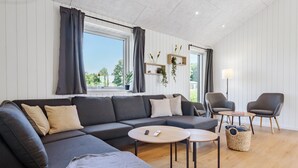 Un salon moderne avec un canapé d’angle, deux petites tables rondes et une table d’appoint.