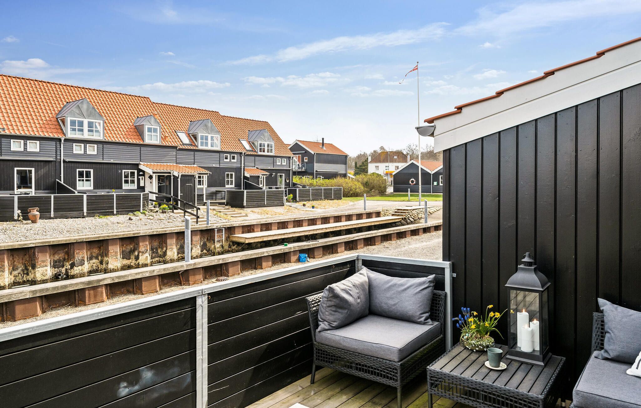 A balcony with a grey sofa, a small table with a lantern, and a view of a railway track and houses in the background.