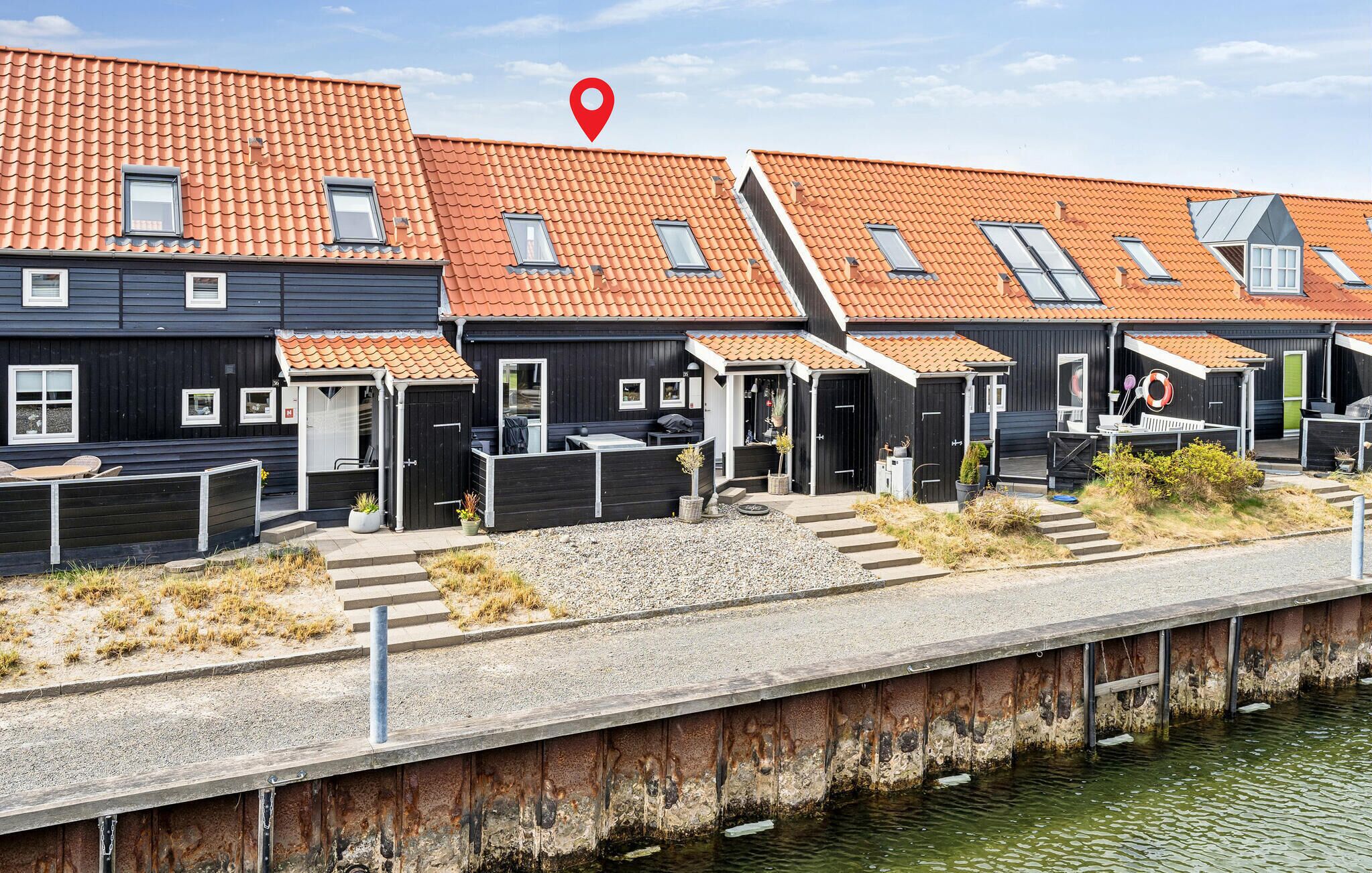 A row of modern, dark-colored buildings with orange-tiled roofs, each with a small window and a door.