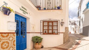 A narrow street with a blue door, a window with metal bars, and potted plants. - Gorgeous home in Cómpeta - Málaga (Cómpeta - Málaga)
