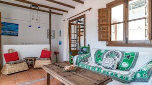 A cozy room with a wooden table, a green and white sofa, and a large window with wooden shutters. - Gorgeous home in Cómpeta - Málaga (Cómpeta - Málaga)