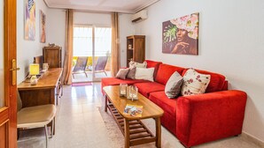 A living room with a red sofa, a wooden coffee table, and a dining area with a wooden table and chairs. There is a sliding glass door leading to an outdoor area with chairs. - Pet friendly apartment in Torrevieja with WiFi (Torrevieja)