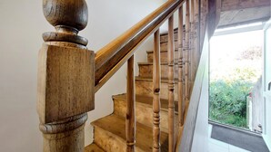 A wooden staircase with a balustrade, leading to an outdoor area visible through a glass door.