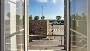 A view through a window of a building with a stone wall, a pedestrian crossing, and parked cars in the background.