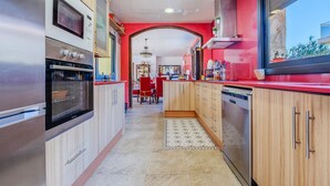 A modern kitchen with stainless steel appliances, wooden cabinets, and a red accent wall. - Pet friendly home in Segur de Calafell (Segur de Calafell)