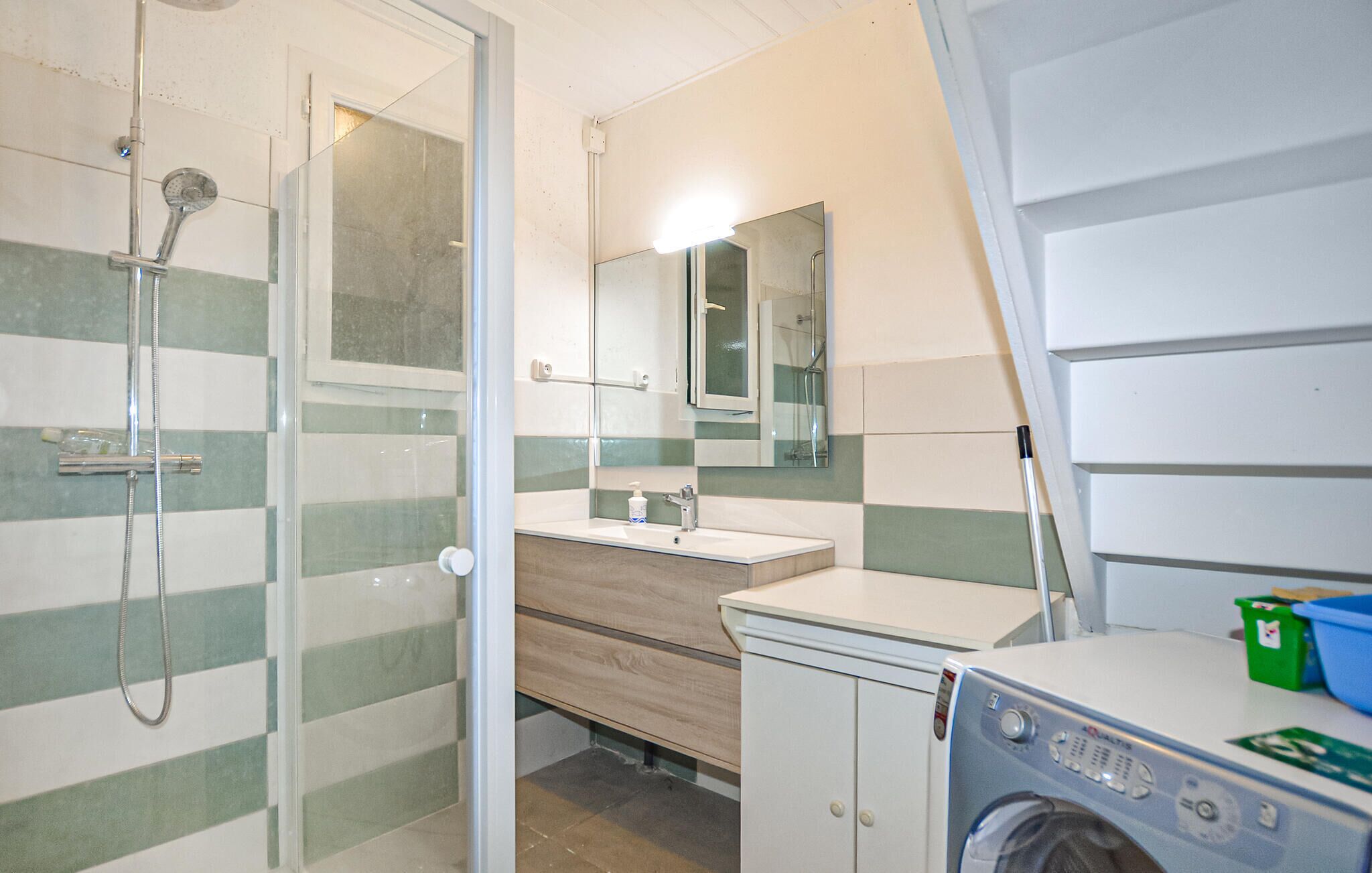 A compact bathroom with a shower, a sink, a mirror, and a washing machine.