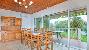 A dining area with a wooden table and chairs, a wooden cabinet, and a glass door leading to a balcony with a view of greenery and a palm tree. - Awesome home in Moriani plage with outdoor swimming pool (Moriani plage)