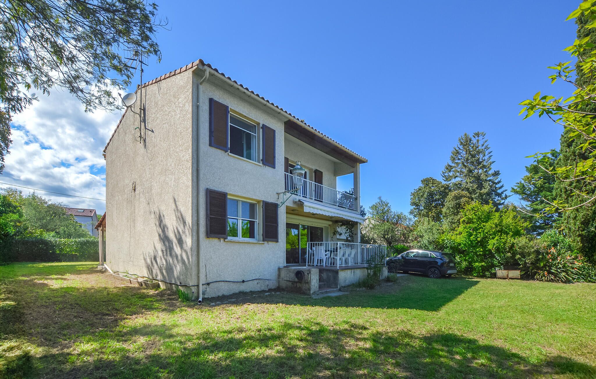 A two-story house with a balcony, a car parked in the driveway, and a lawn.