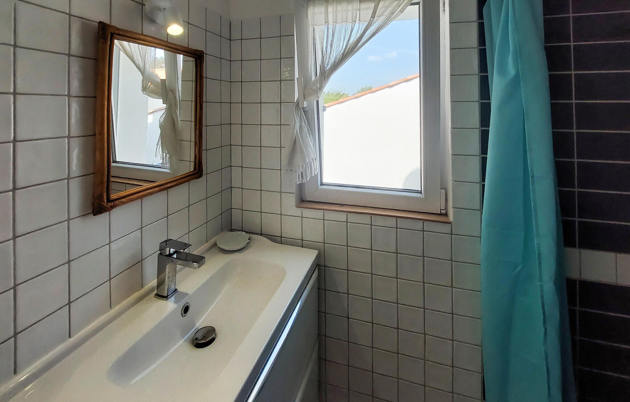 A bathroom with a white sink, a mirror, and a window with curtains.