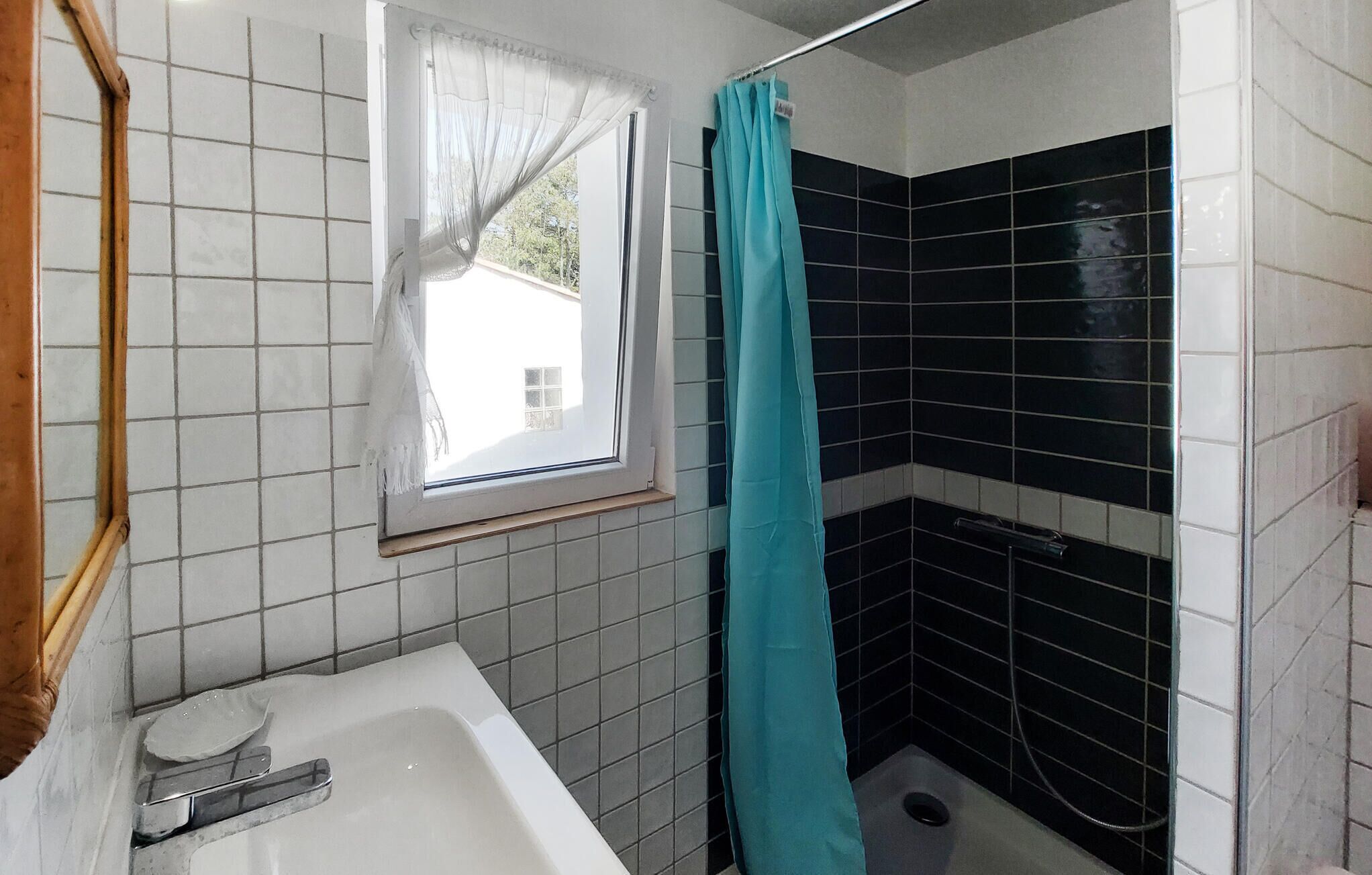 A bathroom with a bathtub, a window with a sheer curtain, and black and white tiled walls.