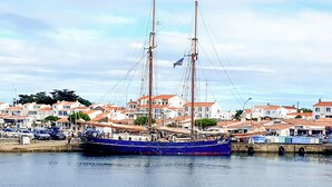 Un vaixell de vela tradicional amarrat a un port, amb edificis residencials al fons.