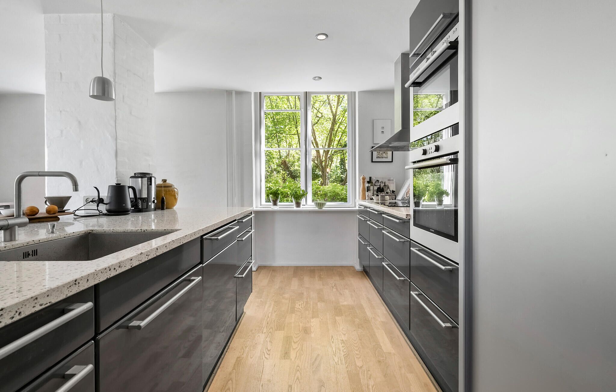 Uma cozinha moderna com uma janela grande, eletrodomésticos de aço inoxidável e piso de madeira.