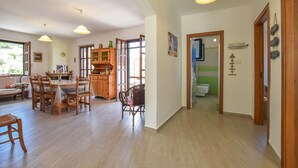A spacious living area with a wooden dining table, chairs, and a sofa. There is a kitchen area with cabinets and a window. The room has wooden flooring and pendant lights. - Amazing home in Perdifumo (Perdifumo)